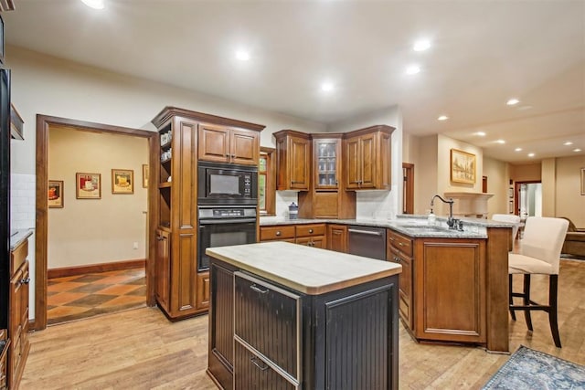 kitchen with a peninsula, a kitchen island, brown cabinets, a sink, and black appliances