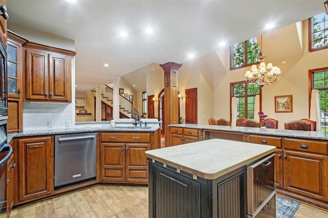 kitchen featuring stainless steel dishwasher, brown cabinetry, a peninsula, a sink, and light wood-style flooring