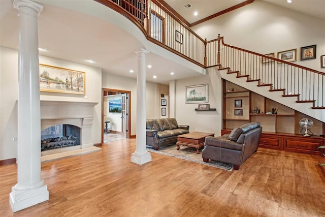 living area featuring ornate columns, a high ceiling, recessed lighting, and wood finished floors