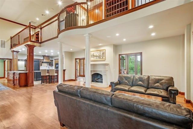 living area featuring visible vents, a towering ceiling, a fireplace with raised hearth, ornate columns, and recessed lighting