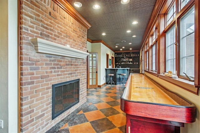 game room featuring crown molding, a fireplace, baseboards, recessed lighting, and a community bar