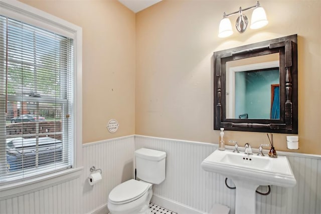 half bathroom with plenty of natural light, a sink, a wainscoted wall, and toilet