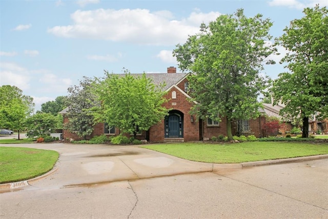 view of front of home featuring a chimney, driveway, a front lawn, and brick siding