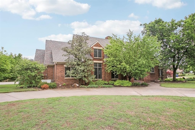 view of front facade featuring roof with shingles, driveway, a front lawn, and brick siding
