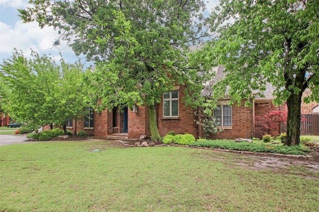 view of property hidden behind natural elements featuring brick siding and a front lawn