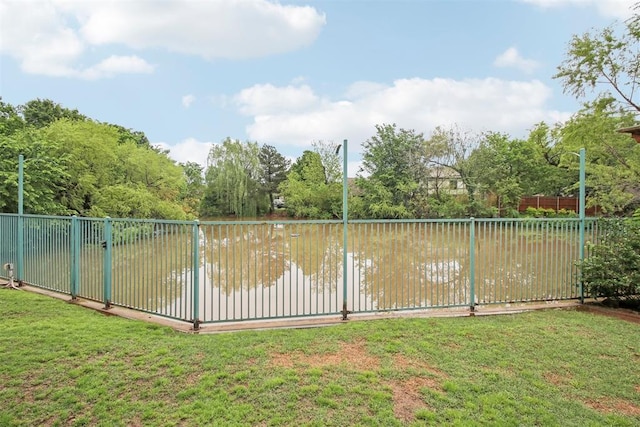 view of swimming pool with fence, a water view, and a lawn