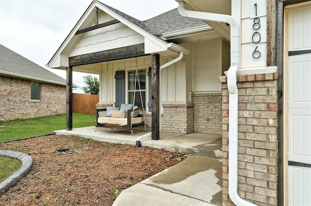 property entrance with board and batten siding, covered porch, roof with shingles, brick siding, and fence