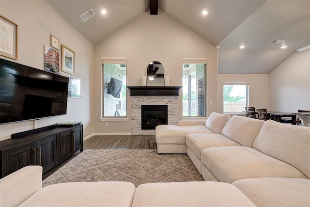 living area featuring a ceiling fan, a stone fireplace, visible vents, wood finished floors, and vaulted ceiling with beams