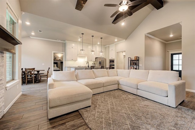 living room featuring a ceiling fan, visible vents, wood finished floors, baseboards, and vaulted ceiling with beams