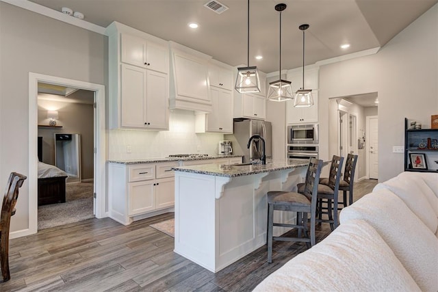 kitchen with appliances with stainless steel finishes, white cabinetry, wood finished floors, a kitchen bar, and visible vents