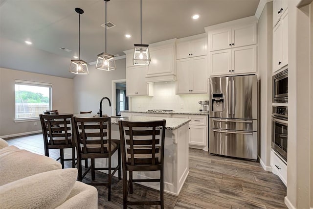 kitchen with white cabinets, stainless steel appliances, wood finished floors, tasteful backsplash, and a center island with sink