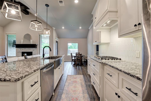 kitchen featuring visible vents, appliances with stainless steel finishes, a fireplace, lofted ceiling with beams, and dark wood-type flooring