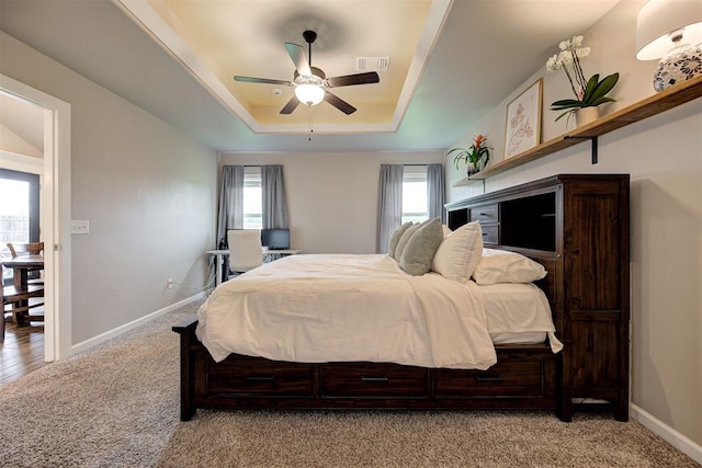 carpeted bedroom featuring baseboards, a ceiling fan, a tray ceiling, and visible vents