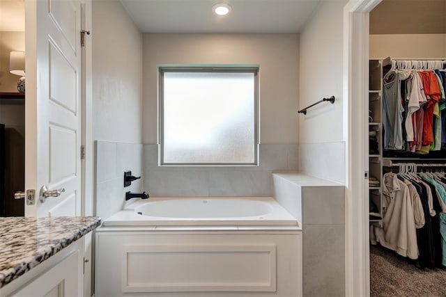 bathroom with recessed lighting, a walk in closet, a garden tub, and vanity