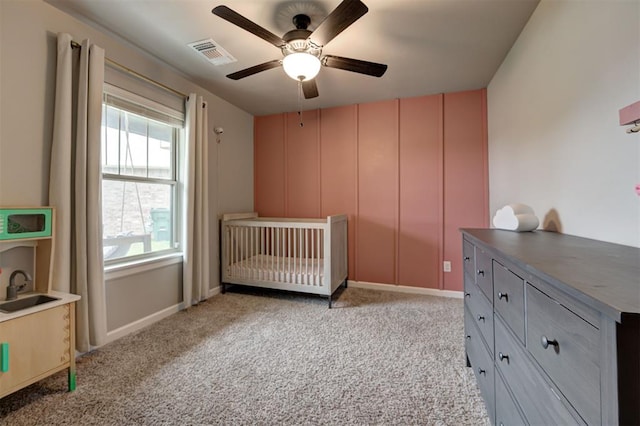 bedroom with a nursery area, ceiling fan, visible vents, and light carpet