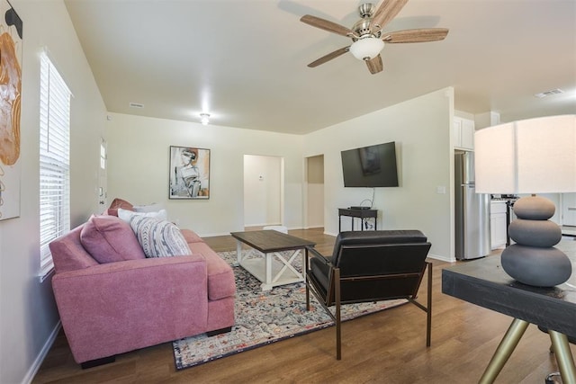 living room featuring visible vents, a ceiling fan, baseboards, and wood finished floors