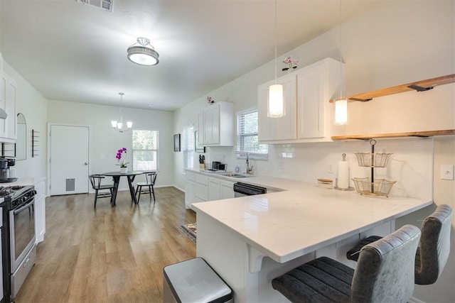 kitchen featuring white cabinets, a sink, stainless steel gas range oven, a breakfast bar area, and light wood-style flooring