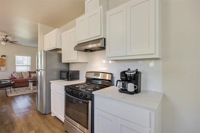 kitchen with decorative backsplash, exhaust hood, a ceiling fan, wood finished floors, and stainless steel appliances