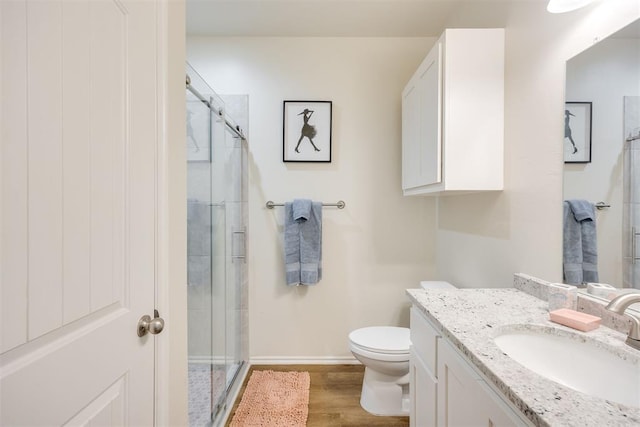 bathroom featuring vanity, toilet, baseboards, wood finished floors, and a stall shower