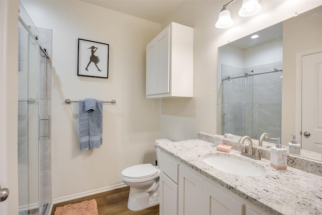 bathroom featuring vanity, wood finished floors, toilet, baseboards, and a shower stall