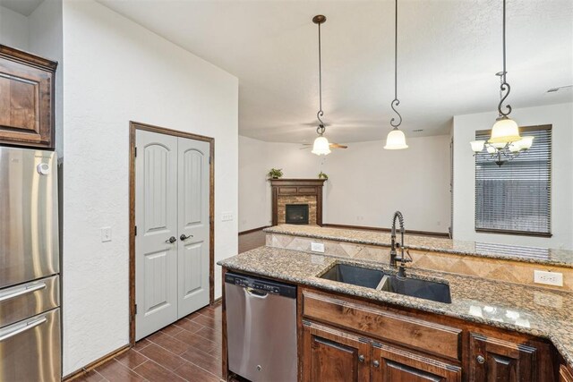 kitchen featuring dark wood-type flooring, a fireplace with raised hearth, light stone counters, a sink, and stainless steel appliances