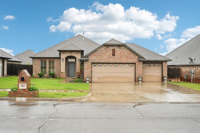 french country style house featuring fence, a front yard, brick siding, a shingled roof, and driveway