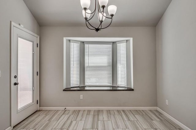 unfurnished dining area featuring baseboards, plenty of natural light, and a chandelier