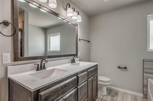 bathroom featuring double vanity, toilet, baseboards, and a sink