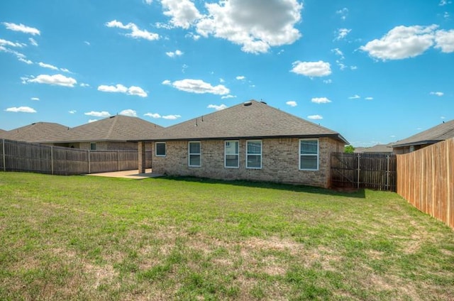 rear view of property featuring a lawn, brick siding, a fenced backyard, and a patio area