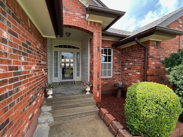 doorway to property with roof with shingles and brick siding
