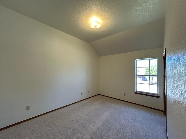 unfurnished room with baseboards, vaulted ceiling, a textured ceiling, and light colored carpet
