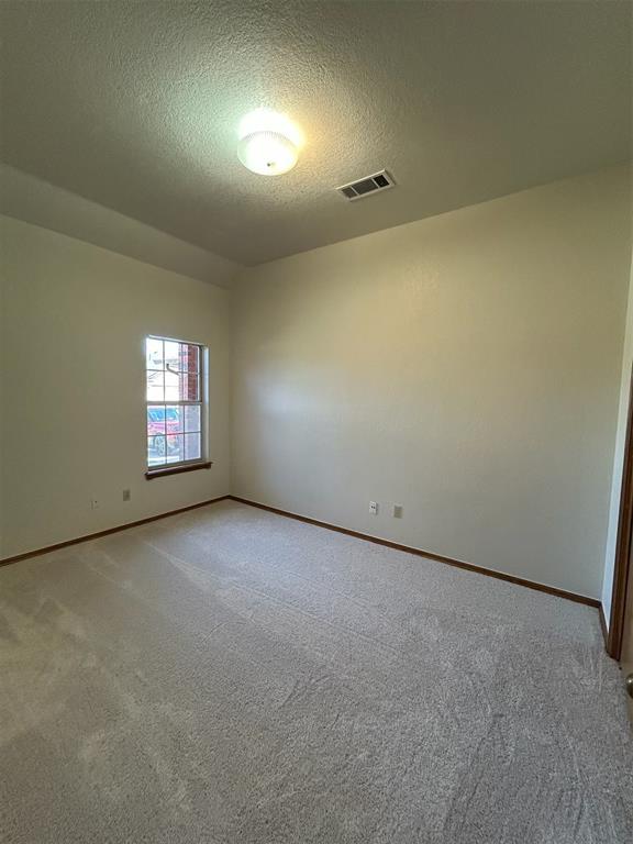 empty room with light colored carpet, a textured ceiling, visible vents, and baseboards