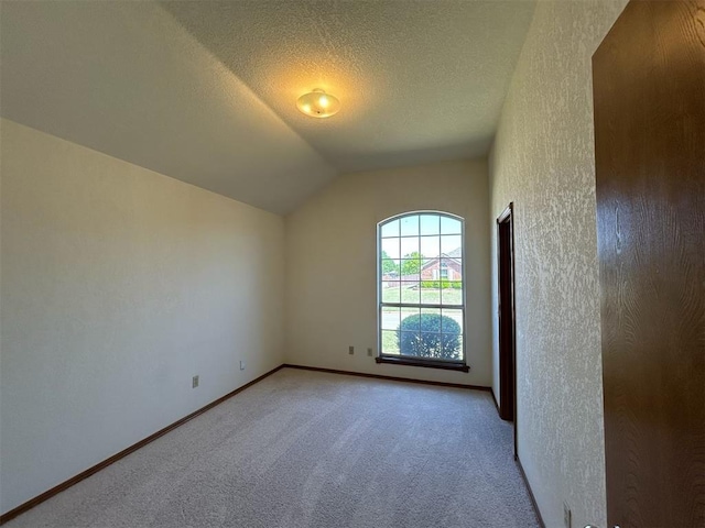 spare room featuring a textured ceiling, baseboards, vaulted ceiling, and light carpet