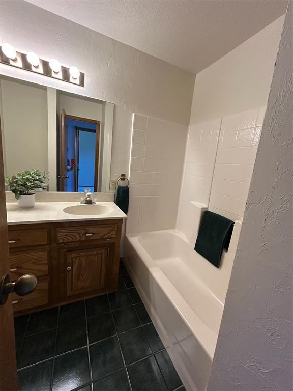 full bath with a textured ceiling, a textured wall, tile patterned floors, and vanity