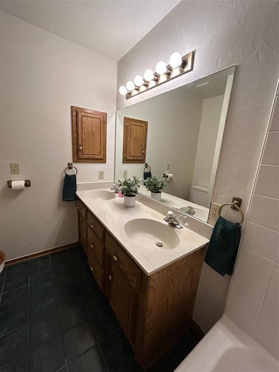 bathroom with double vanity, toilet, a textured ceiling, tile patterned floors, and a sink