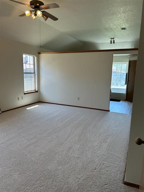 carpeted spare room featuring baseboards, a ceiling fan, lofted ceiling, and visible vents