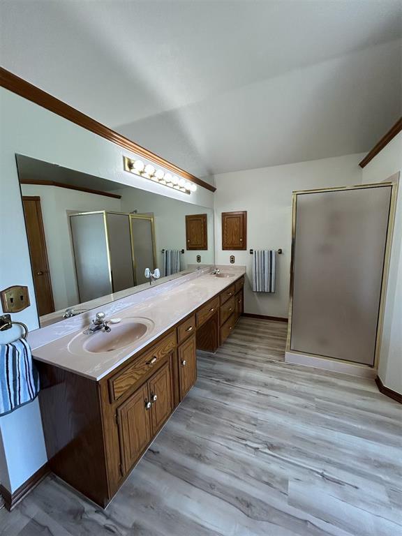 full bathroom with a sink, double vanity, wood finished floors, lofted ceiling, and a stall shower