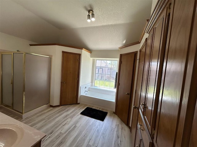 full bathroom with a garden tub, a textured ceiling, a shower stall, wood finished floors, and lofted ceiling