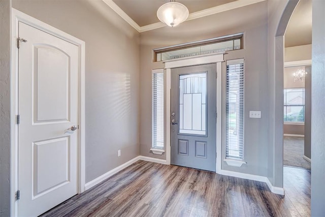 foyer with baseboards, ornamental molding, arched walkways, and wood finished floors