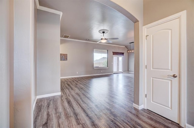 unfurnished room featuring a ceiling fan, arched walkways, wood finished floors, baseboards, and ornamental molding