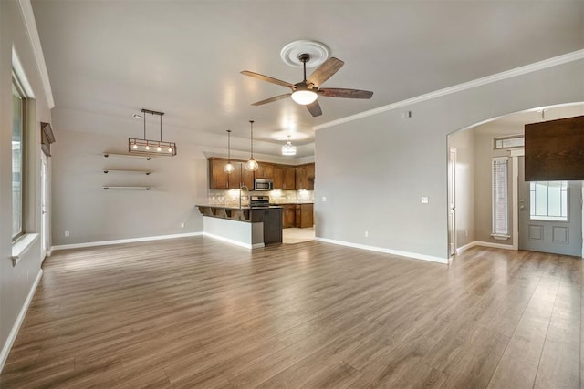 unfurnished living room featuring arched walkways, baseboards, ceiling fan, and wood finished floors