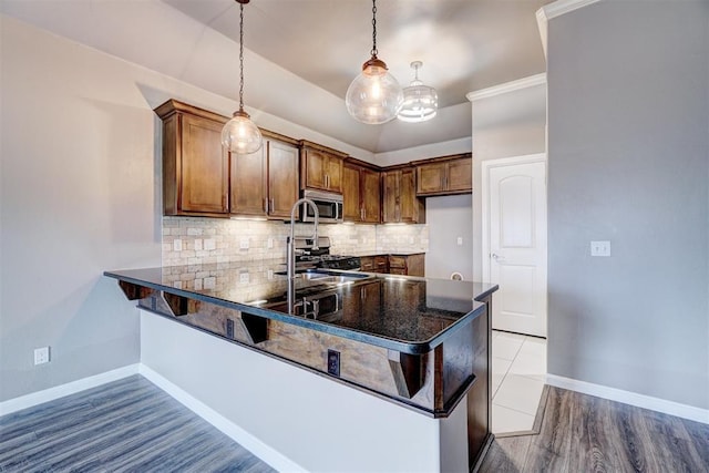 kitchen with decorative backsplash, a sink, baseboards, a peninsula, and stainless steel appliances