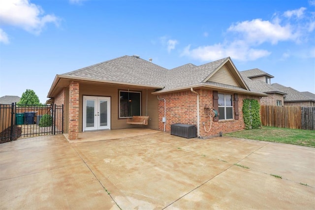 rear view of property with a fenced backyard, french doors, brick siding, a shingled roof, and a patio area