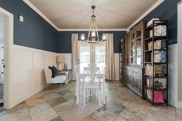 dining area with a decorative wall, a chandelier, crown molding, and a wainscoted wall