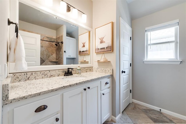 full bath with a tile shower, vanity, and baseboards