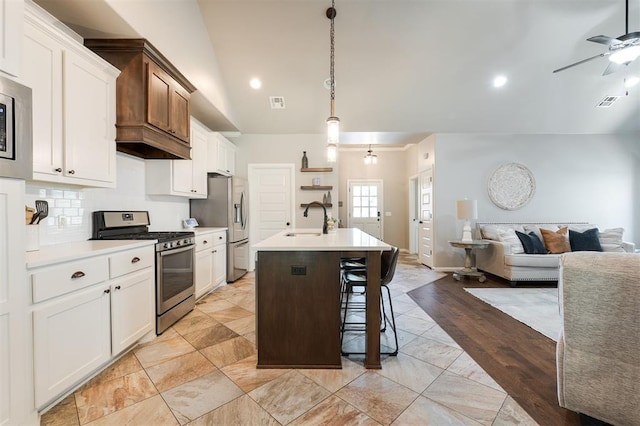 kitchen featuring stainless steel appliances, a sink, open floor plan, ceiling fan, and an island with sink