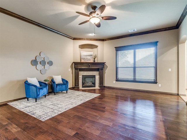 living area with a ceiling fan, visible vents, wood finished floors, a glass covered fireplace, and ornamental molding