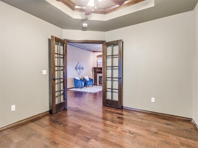 unfurnished room with a ceiling fan, french doors, wood finished floors, ornamental molding, and a tray ceiling