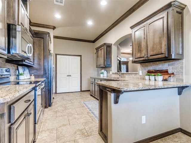 kitchen with crown molding, appliances with stainless steel finishes, tasteful backsplash, and a kitchen bar