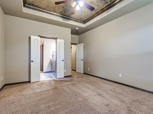 unfurnished bedroom featuring carpet flooring, a tray ceiling, baseboards, and ensuite bath